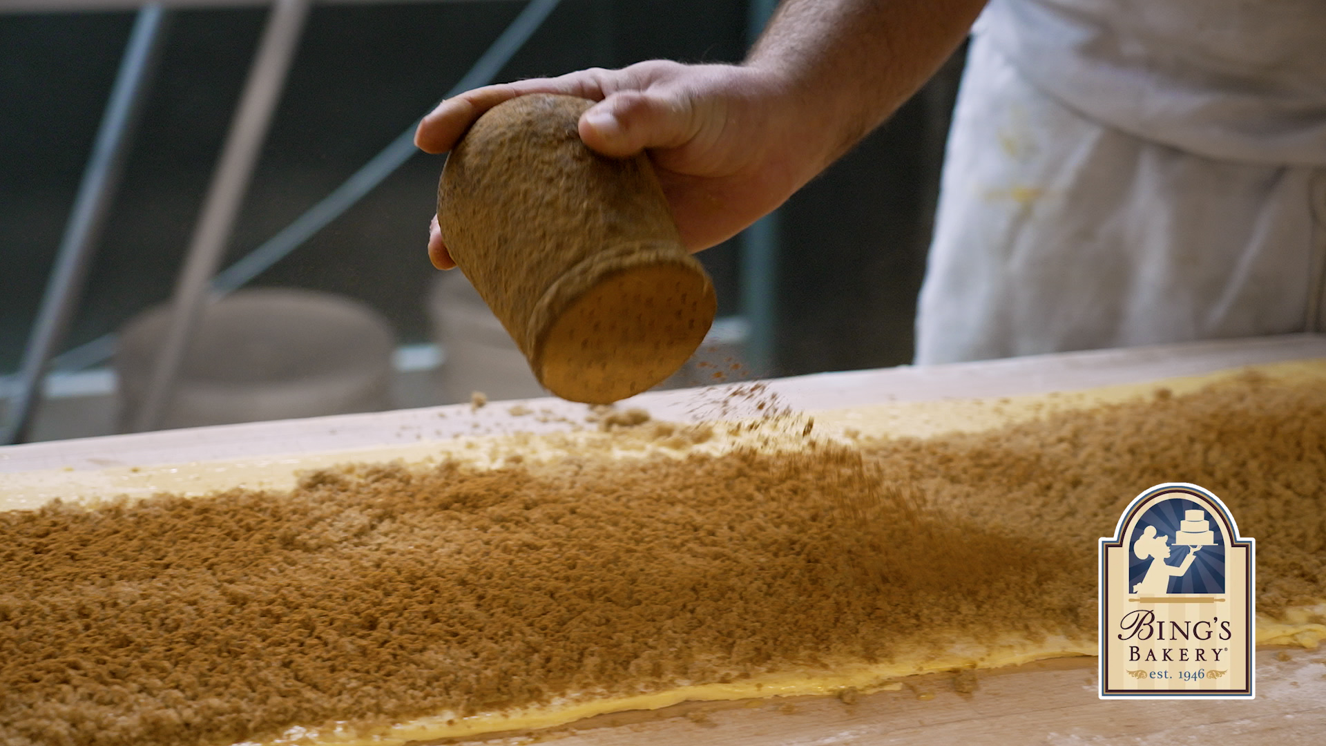 Baker dusting cinnamon sugar over dough during the overnight shift at Bings Bakery